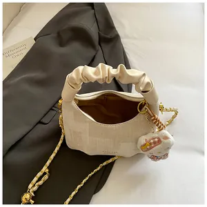 Beige pleated handbag with gold chain strap and cartoon cat charm on grey blazer