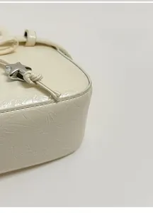 Detailed close-up of beige patent leather bag with star metal stud and stitching