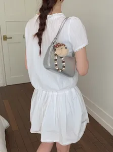 Silver metallic shoulder bag with cute plush mushroom charm shown on a female model