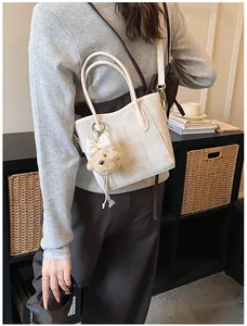 Detail of off-white canvas crossbody bag with cute plush bear and bow keychain detail