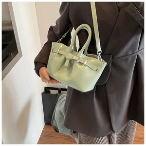 Detail of mint green glossy bucket bag with buckle strap on model in indoor setting