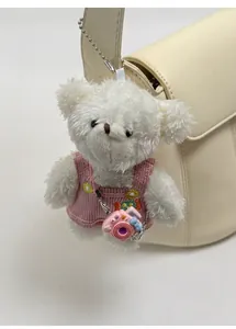 Close-up of white plush bear pendant with pink knitted overalls on a bucket bag