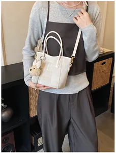 Chic beige textured shoulder bag with a cute bear charm, styled on a female model