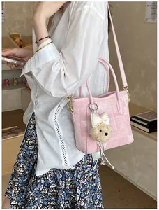 Detail of pink woven tote bag with cute plush bear charm and crossbody strap