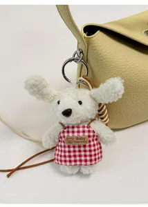 Close-up of white plush lamb wool puppy charm with red checkered apron on a handbag