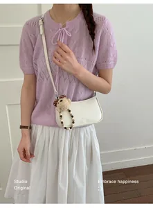 Detail of cream half-moon bag with plush bear charm and beaded strap on a model