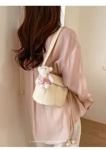 Detail view of cream bucket bag with plush bear charm worn by model in casual setting