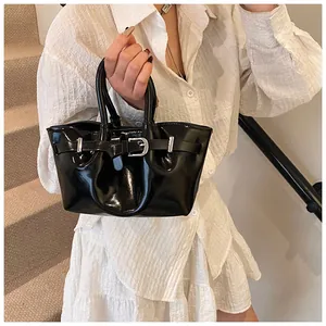 Detail of glossy black bucket bag with buckle strap and pleated texture shown on model