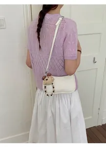 Detailed close-up of a white PU leather crescent bag with a cute teddy bear charm