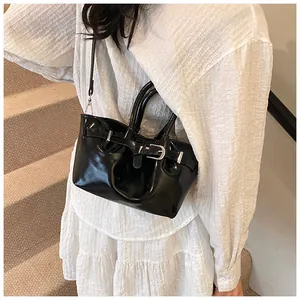 Polished black bucket bag with buckle detail worn by a model on a staircase