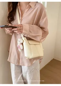 Close-up of minimalist beige bucket bag with vertical stitching and plush bear charm