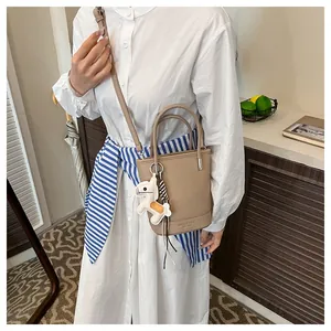 Detail of beige lychee pattern bucket bag with leather handle and horse charm accessory