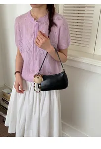 Chic black baguette bag with plush bear charm and beaded detail on a purple knit top