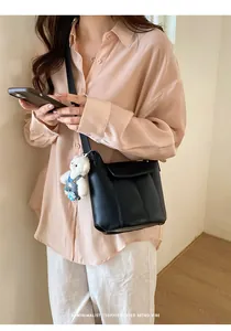 Minimalist black leather bucket bag detail with a cute white plush bear pendant decor
