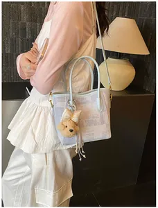 Chic light blue tote bag with plush bear charm worn as a stylish shoulder bag for women