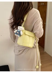 Detail of yellow crossbody bucket bag with stitching and a cute bear plush pendant charm
