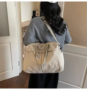 Detail of a large beige travel tote bag with adjustable straps and front pockets