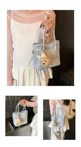 Detail of light blue textured tote bag with detachable strap and plush bear charm accessory