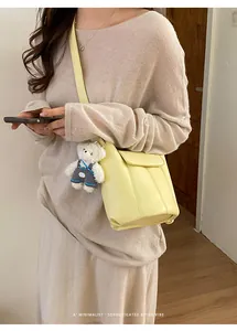 Detail of cream yellow bucket bag with a cute white plush bear charm on the shoulder strap