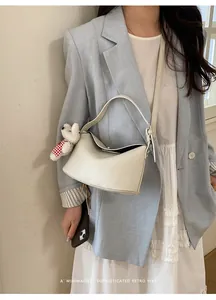Detail of cream white pebbled leather handbag with plush bear charm worn by a model