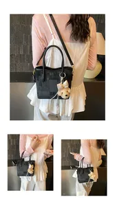 Detail of black textured handbag with detachable shoulder strap and cute teddy bear charm