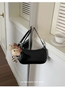 Detail of black matte shoulder bag with a cute brown plush bear charm and beaded accent