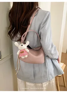 Detail view of pink lychee leather crossbody bag with a cute plush bunny charm on the strap