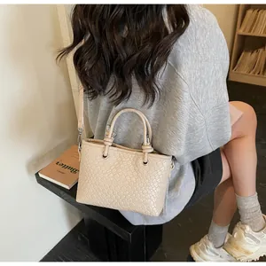 Borsa a secchiello intrecciata beige portata a tracolla da una modella in un interno di stile