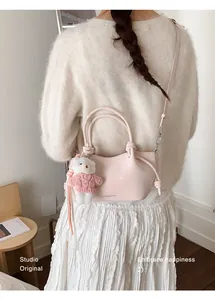 Detail der hellrosa Umhängetasche mit Bärenanhänger getragen zu einem cremefarbenen Pullover