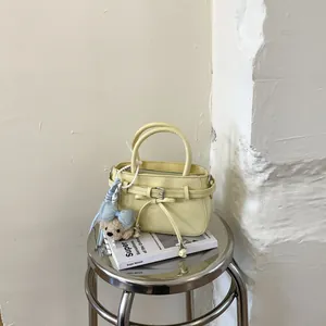 Detail of light yellow mini handbag featuring a blue bow and plush bear charm