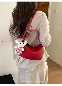 Detail of red lychee pattern crescent bag with white plush puppy charm and straps
