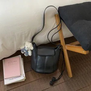 Detail of black leather bucket bag with cute white teddy bear charm and soft tassel