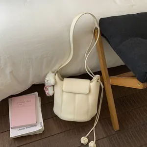 Detail of off-white bucket bag with drawstring knot and plush bear charm on white bedding