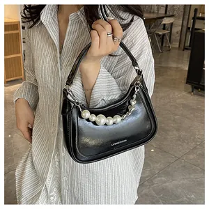 Détail d'un sac à main noir brillant avec une chaîne en perles et un pendentif coeur argent