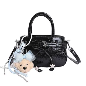 Elegant black patent leather handbag with bow detail and bear charm in white background