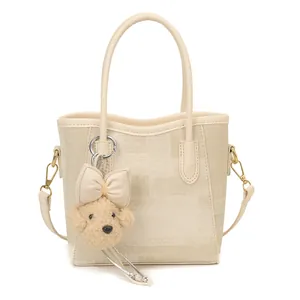 Minimalist cream textured crossbody bag with cylindrical handles and cute plush charm