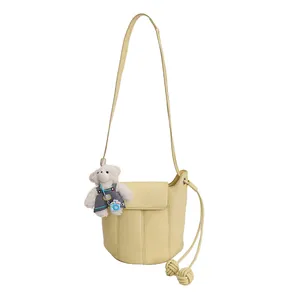 Chic pale yellow leather bucket bag with teddy bear charm and adjustable strap