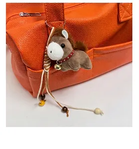 Detail of plush pony charm with red collar and bell on a orange textured tote bag
