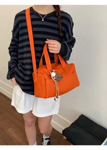 Bright orange PU leather tote bag with horse pendant worn by a model in a casual setting