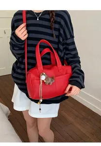 Detail of red pebbled leather tote with horse charm accessory worn by model