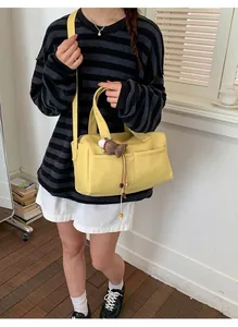 Detail of yellow tote bag featuring dual front pockets and adjustable strap with bear charm