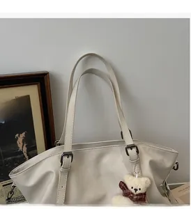 Detail of cream tote bag featuring adjustable retro metal buckles and a cute teddy bear charm
