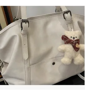 Detail of cream tote bag with fine stitching, adjustable strap, and plush bear charm