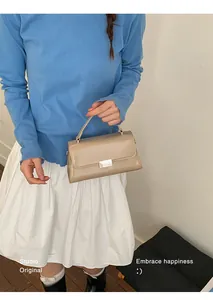 Detail of a beige glossy mini crossbody bag with silver buckle held by a model