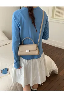 Detail of a beige PU leather crossbody bag featuring a silver rectangular metal lock