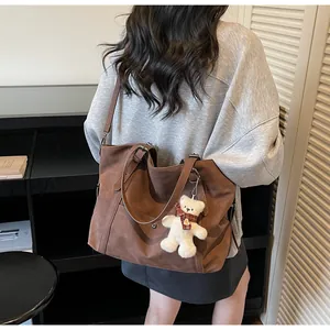 Detail of a large brown suede tote bag with a plush bear charm and adjustable strap