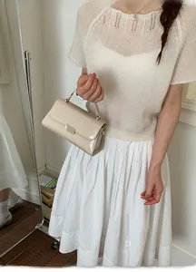 Detail of a beige leather handbag with silver metallic buckle on a white knit outfit