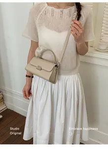 Chic cream leather handbag with silver lock shown on a white pleated dress backdrop