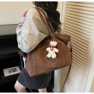 Brown leather tote bag with teddy bear charm shown as a shoulder bag on a model