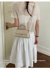 Detail of a creamy beige square crossbody bag with metal buckle on a fashion model